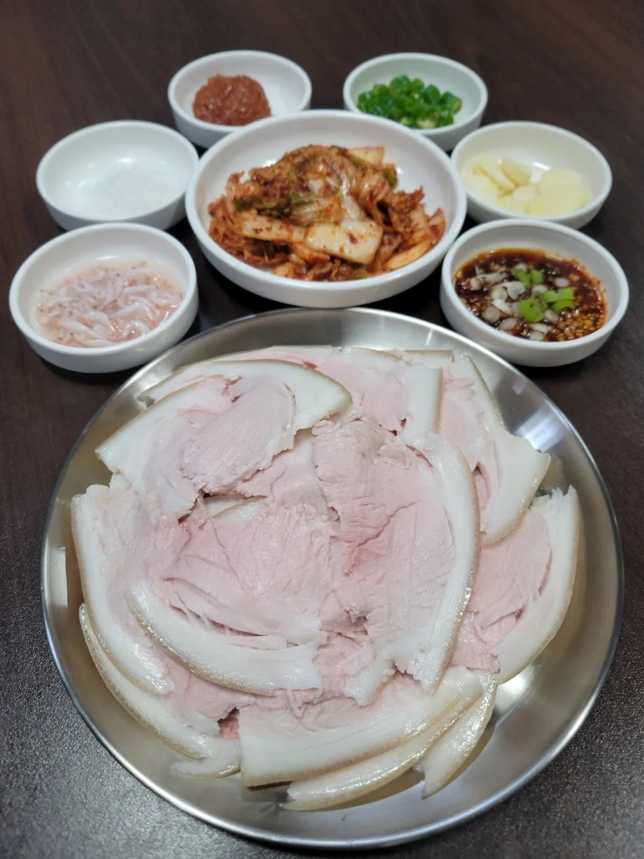 잔치수육 한 접시와 김치, 새우젓·마늘·고추·간장 양념 종지