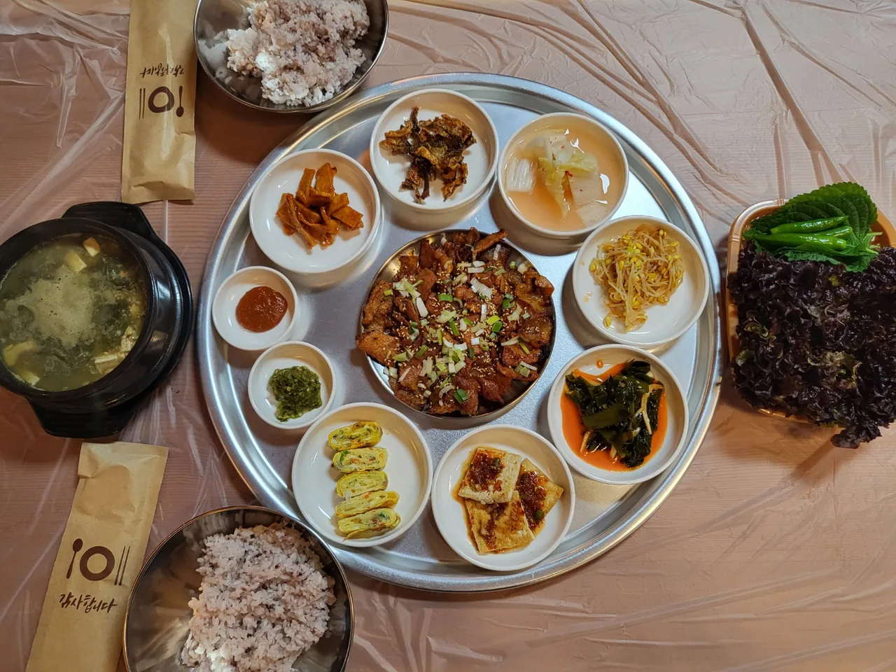 위에서 본 연탄고추장불고기 상차림 — 둥근 쟁반 가운데 불고기와 둘레 반찬, 왼쪽 뚝배기, 밥 두 공기, 오른쪽 쌈채소
