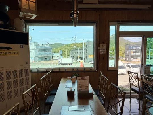 창가 자리 — 긴 나무 탁자와 금색 의자, 큰 창 너머 거리와 산